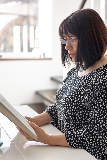 Foto gratuita una mujer morena de mediana edad con gafas y un corte de pelo bob está leyendo un libro