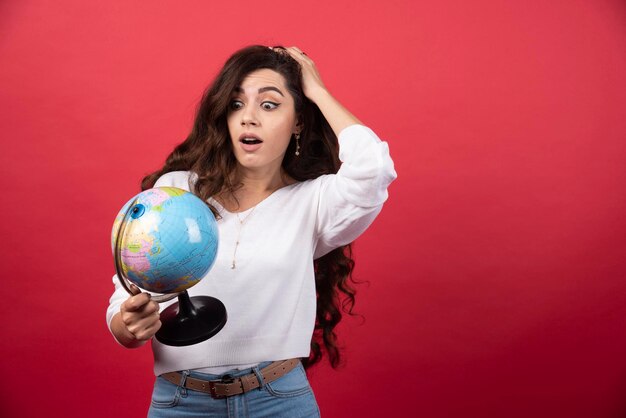 Mujer morena mirando globo sobre fondo rojo. Foto de alta calidad