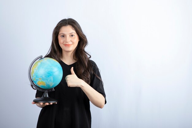 Mujer morena con pelo largo sosteniendo globo terráqueo y posando.