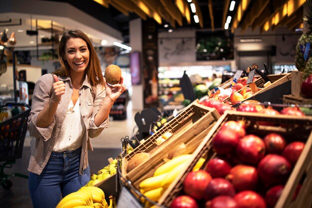 Mujer morena positiva sosteniendo coco en el departamento de frutas de la tienda de comestibles