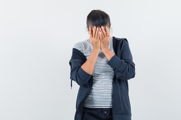 Mujer morena que cubre el rostro con las manos en camisa