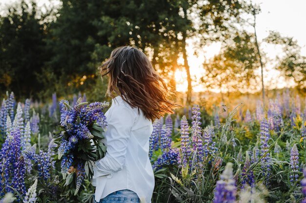 Mujer morena remolinos con ramo de lupinos en un césped en puesta de sol