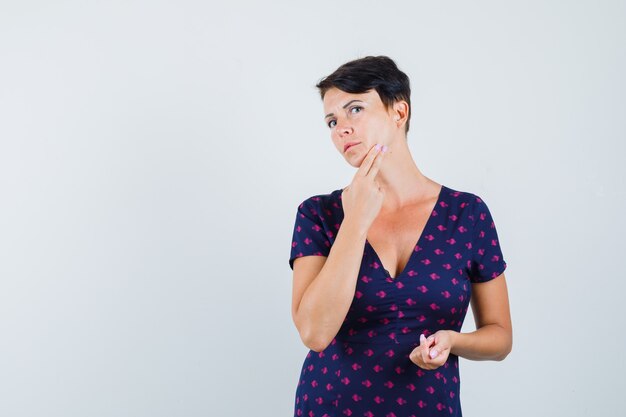 Mujer morena revisando su rostro en vestido estampado morado y rojo y mirando enfocado. vista frontal.