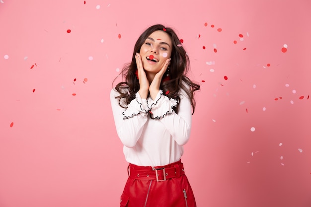 Mujer morena se ríe sobre fondo rosa con confeti. Retrato de niña en falda roja.