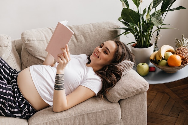 Mujer morena rizada en camiseta blanca y pantalón lee libro