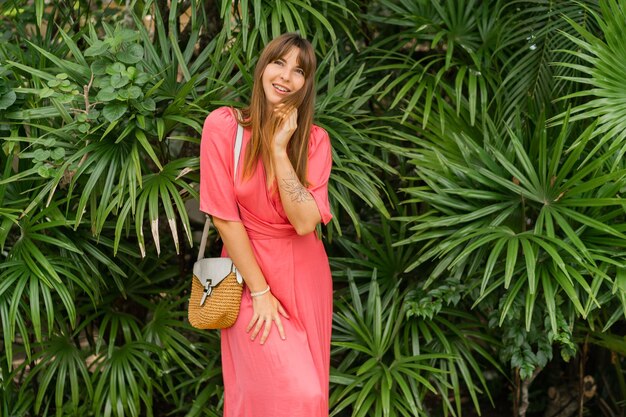 Mujer morena romántica en elegante vestido rosa disfrutando de vacaciones tropicales