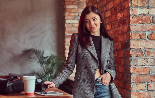 Mujer morena sensual vestida con ropa de moda posando en una habitación con interior de loft, mirando a la cámara.