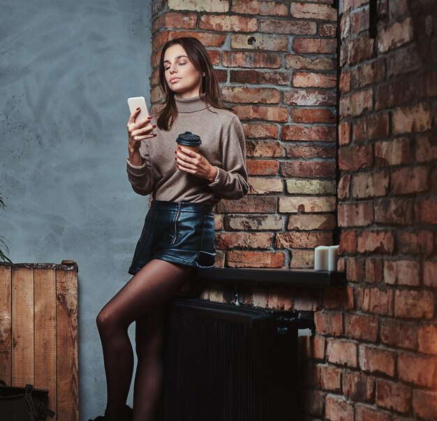 Mujer morena sexy usando un teléfono inteligente en una habitación con interior de loft.