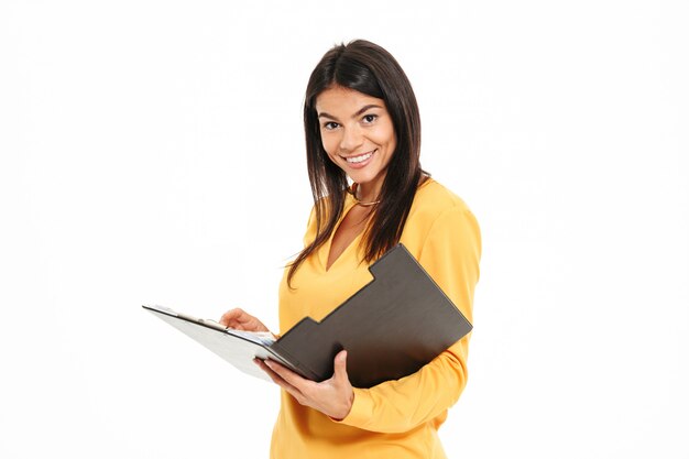 Mujer morena sonriente en camisa amarilla con portapapeles