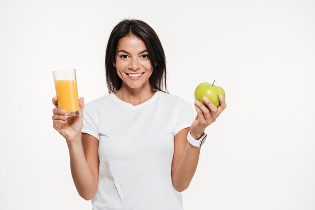 Mujer morena sonriente que sostiene el vidrio de un jugo de naranja