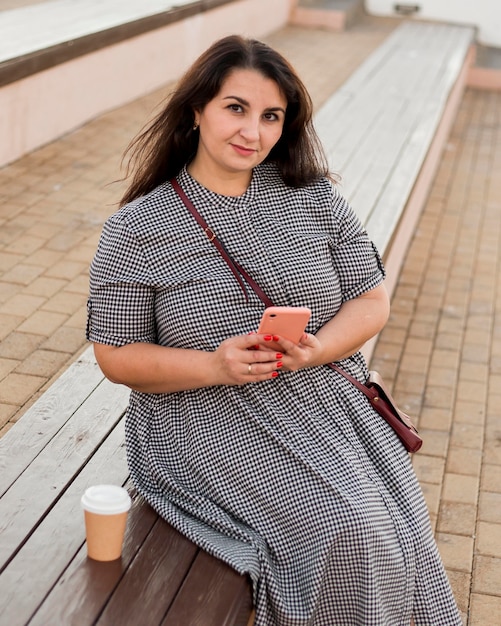 Mujer morena sonriente sosteniendo su smartphone al aire libre