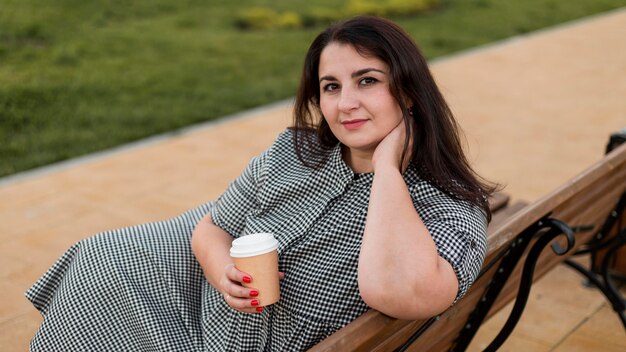 Mujer morena sonriente sosteniendo una taza de café al aire libre