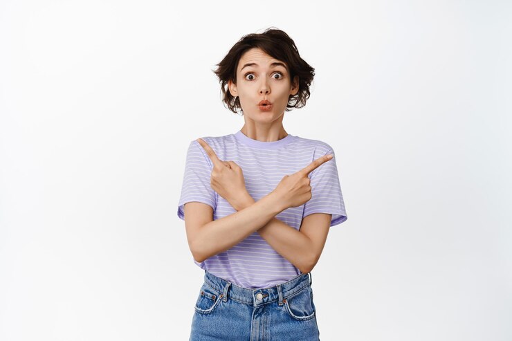 Foto gratuito mujer morena sorprendida y emocionada que muestra dos lados, apuntando hacia los lados a izquierda y derecha, dice wow y mirando impresionada a la cámara, parada sobre fondo blanco