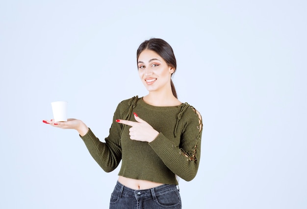 Foto gratuita mujer morena sosteniendo un vaso de plástico y apuntando a él.