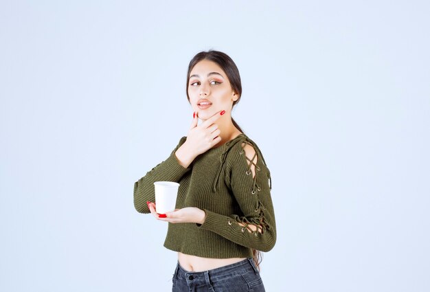 mujer morena sosteniendo un vaso de plástico y pensando.