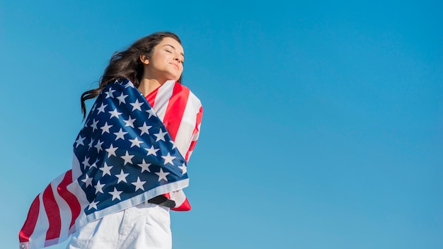 Mujer morena de tiro medio sosteniendo gran bandera de Estados Unidos y sonriendo