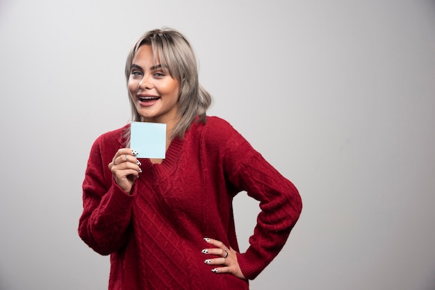 Mujer mostrando bloc de notas sobre fondo gris.