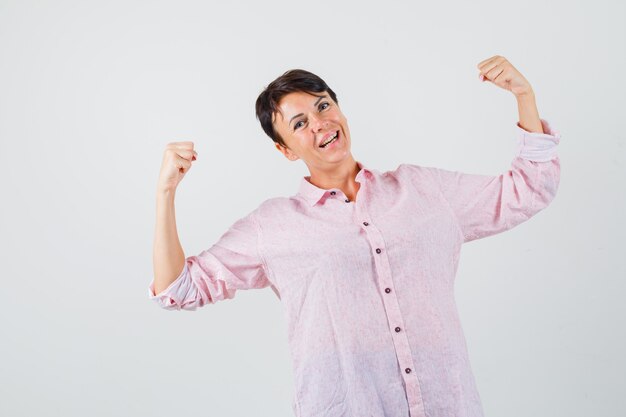 Mujer mostrando gesto de ganador en camisa rosa y con suerte, vista frontal.