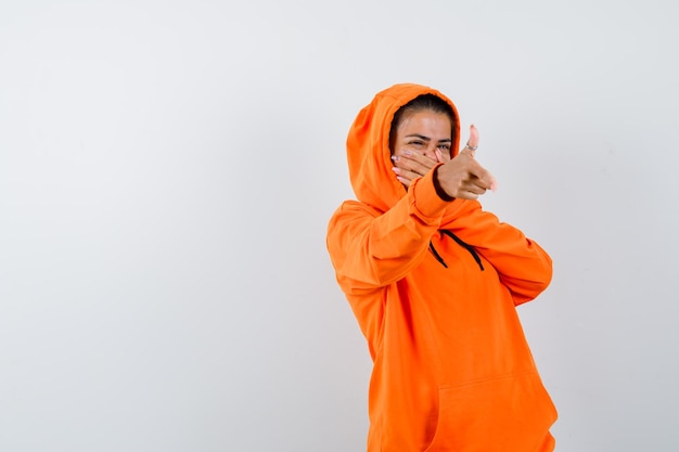 Mujer mostrando gesto de pistola en sudadera con capucha naranja y mirando feliz