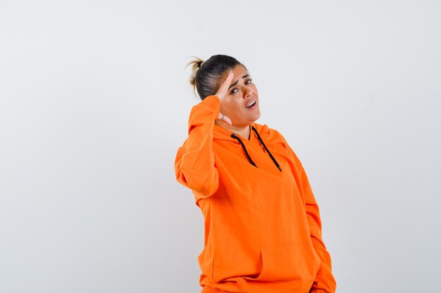 Mujer mostrando gesto de saludo en sudadera con capucha naranja y mirando confiado