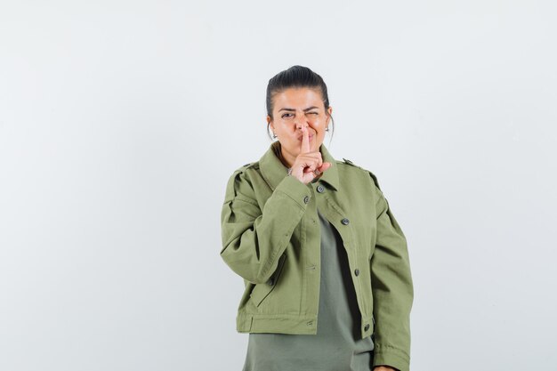 mujer mostrando gesto de silencio en chaqueta, camiseta y mirando confiado.