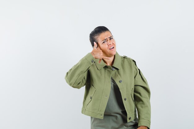 Mujer mostrando gesto de teléfono en chaqueta, camiseta y mirando confiado