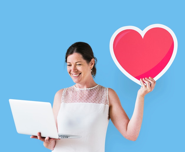 Mujer mostrando un icono de corazón y usando una laptop