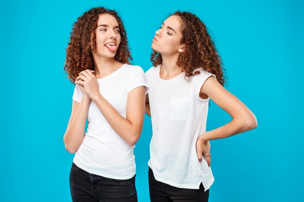 mujer mostrando lengua su hermana gemela sobre pared azul