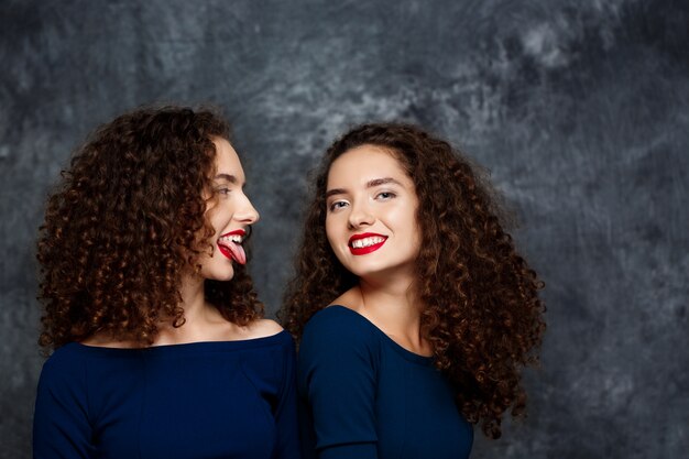 Mujer mostrando lengua su hermana gemela sonriendo en gris