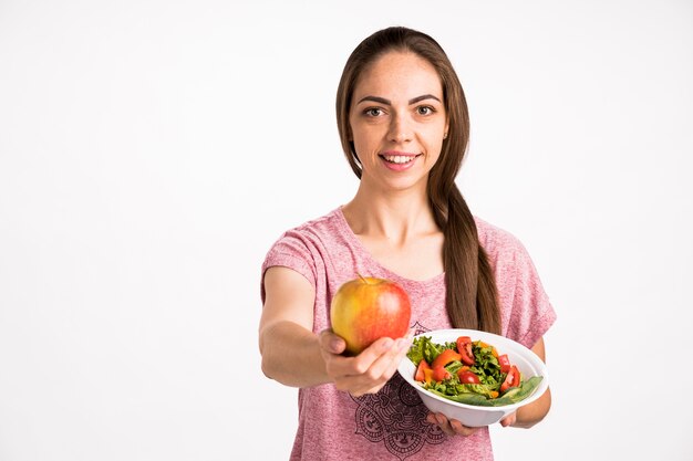 Mujer mostrando una manzana y sosteniendo una ensalada