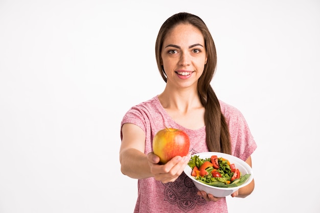 Mujer mostrando una manzana y sosteniendo una ensalada