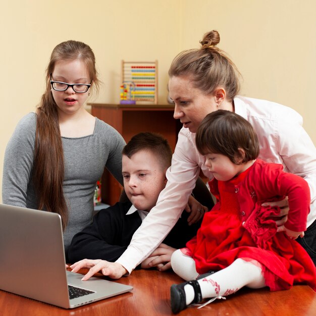 Mujer mostrando a los niños con síndrome de Down algo en la computadora portátil