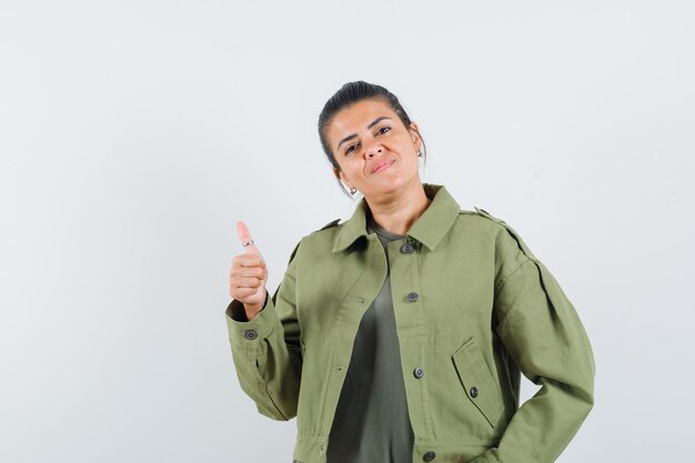 Mujer mostrando el pulgar hacia arriba en chaqueta, camiseta y mirando complacido