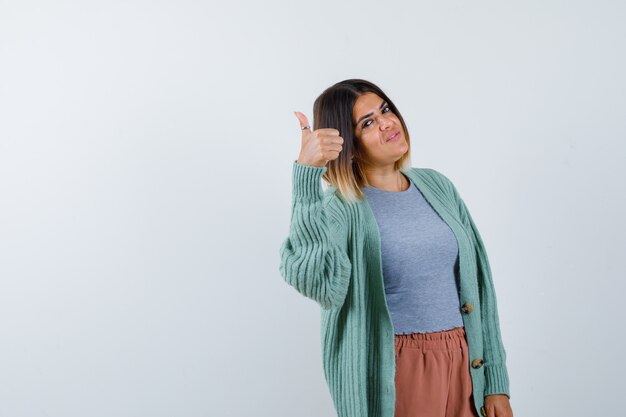 Mujer mostrando el pulgar hacia arriba en ropa casual y mirando confiado, vista frontal.