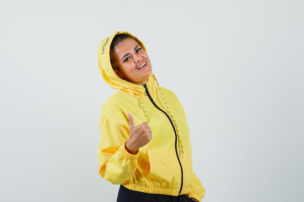 Mujer mostrando el pulgar hacia arriba en traje deportivo y mirando confiada. vista frontal.