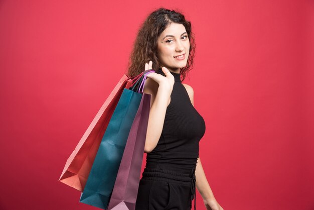 Mujer mostrando su nueva compra de ropa sobre fondo rojo. Foto de alta calidad