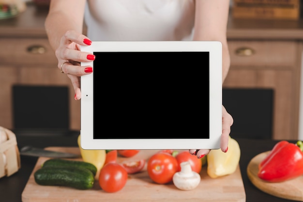 Mujer mostrando tableta digital sobre las verduras crudas en tajadera