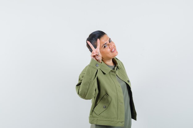 mujer mostrando V-sign en chaqueta, camiseta y luciendo alegre.