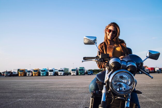 Mujer motociclista en chaqueta de cuero sentado en moto retro y sonriendo