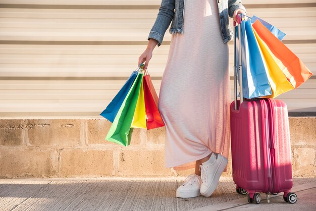 Mujer con muchos bolsos de compras brillantes y maleta