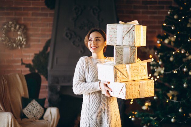 Mujer con muchos regalos delante de arbol de navidad.