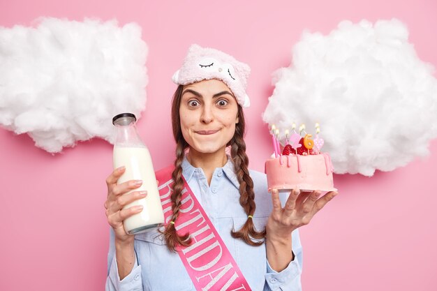 mujer muerde los labios y mira con ternura tiene ganas de comer un delicioso pastel de cumpleaños con leche disfruta celebrando cumpleaños en un ambiente doméstico posa interior. Concepto de vacaciones