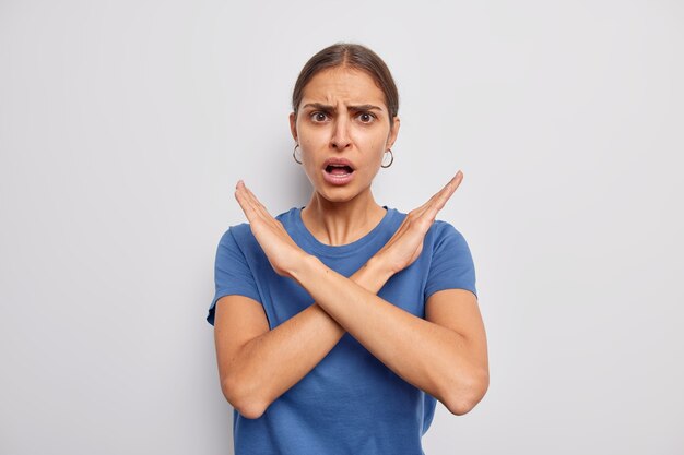 La mujer muestra el gesto de parada cruzada dice que no prohíbe una mala acción rechaza algo viste una camiseta azul informal demuestra un signo de tabú en blanco