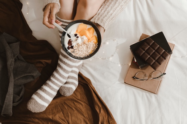 Mujer de mujer de cultivo desayunando cerca de libros y chocolate