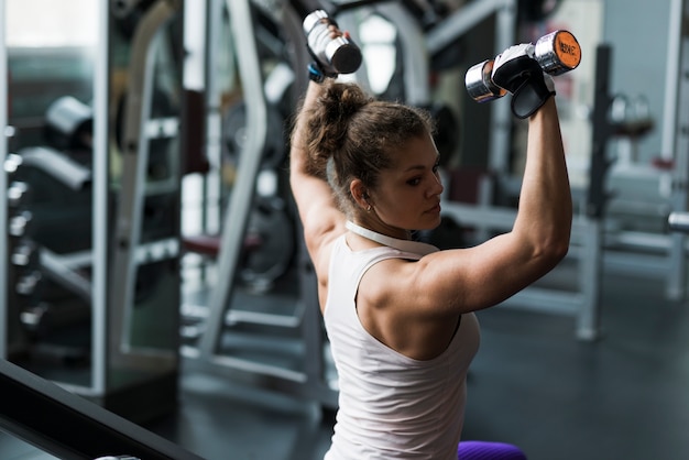 Mujer muscular que ejercita con pesas de gimnasia