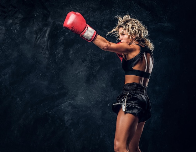 Mujer musculosa deportiva está demostrando sus ejercicios de boxeo, usando guantes.