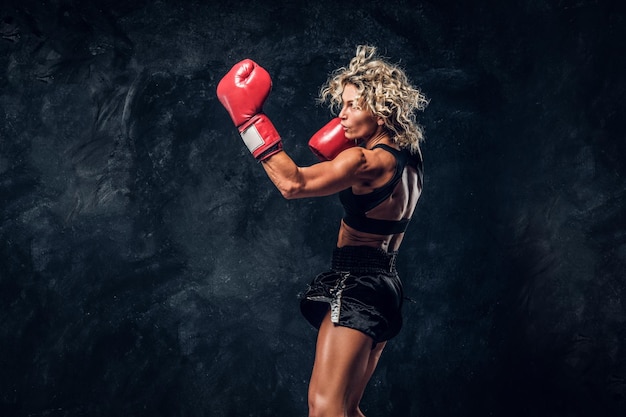 Mujer musculosa deportiva está demostrando sus ejercicios de boxeo, usando guantes.