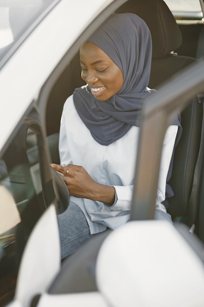 Mujer musulmana africana sentada en su coche y sosteniendo una tableta digital. Trabajar de forma remota o compartir información.