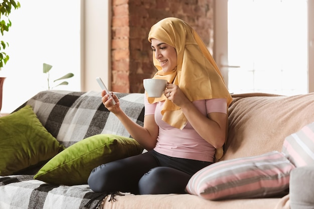 Foto gratuita una mujer musulmana bastante joven en casa durante la cuarentena y el autoaislamiento