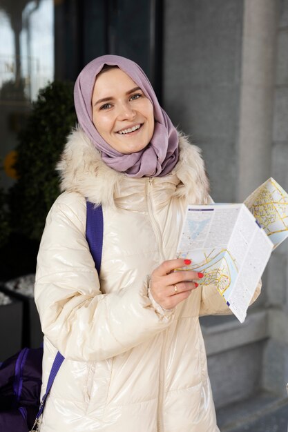 Mujer musulmana consultando un mapa y sonriendo mientras está de vacaciones